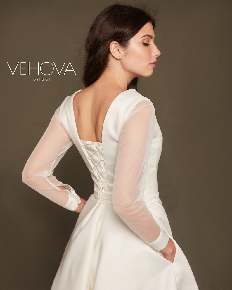 Puede incluir: Un vestido de novia blanco con la espalda de encaje y mangas largas transparentes. El vestido tiene un dise&ntilde;o simple y elegante y una falda fluida.