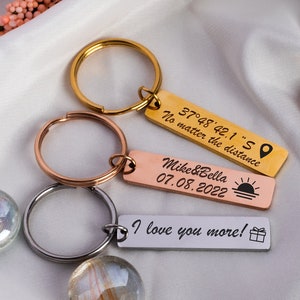 May include: Three gold, rose gold, and silver keychains with engraved messages. The gold keychain says "No matter the distance 37°48′42.1"S". The rose gold keychain says "Mike&Bella 07.08.2022". The silver keychain says "I love you more!"