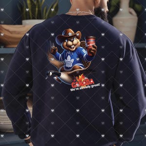 May include: A navy blue sweatshirt featuring a cartoon beaver wearing a Toronto Maple Leafs jersey and holding a Tim Hortons coffee cup. The beaver is riding a Canada goose. The text "CANADA We're already great!" is printed below the graphic.