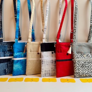 May include: Six crossbody bags in various colors and patterns. The bags have adjustable straps, zippered pockets, and decorative tassels. Colors include denim, blue tie-dye, beige, black and white, red, and gray leopard print.