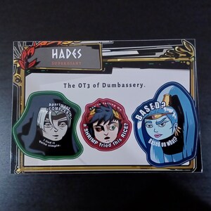 May include: A sheet of stickers featuring characters from the video game Hades. The stickers include character portraits with humorous phrases such as "Apartment Complex? I find it quite simple." and "Based on what?"