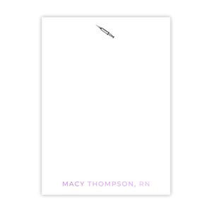 May include: White notepad with a black and white illustration of a syringe at the top and the text "MACY THOMPSON, RN" at the bottom.