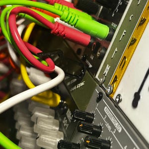 Peut inclure: Gros plan sur un synth&eacute;tiseur modulaire avec un enchev&ecirc;trement de c&acirc;bles color&eacute;s. Des c&acirc;bles verts, rouges, jaunes et blancs sont branch&eacute;s sur l'appareil. L'appareil comporte des boutons et le texte "SQ-1" et "Parametric EQ".