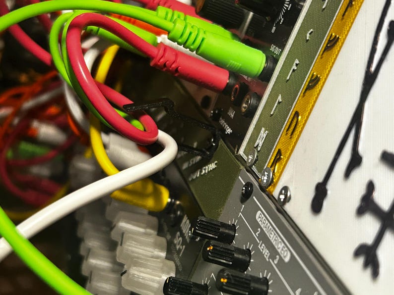 Peut inclure: Gros plan sur un synth&eacute;tiseur modulaire avec un enchev&ecirc;trement de c&acirc;bles color&eacute;s. Des c&acirc;bles verts, rouges, jaunes et blancs sont branch&eacute;s sur l'appareil. L'appareil comporte des boutons et le texte "SQ-1" et "Parametric EQ".