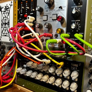 Peut inclure: Gros plan sur un synth&eacute;tiseur modulaire avec divers modules et c&acirc;bles de raccordement color&eacute;s. Les modules comportent des boutons, des interrupteurs et des &eacute;tiquettes textuelles. Des c&acirc;bles rouges, blancs, jaunes et verts relient les modules.