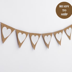 May include: A burlap banner with white heart cutouts. The banner is strung together with twine and has a rustic look.