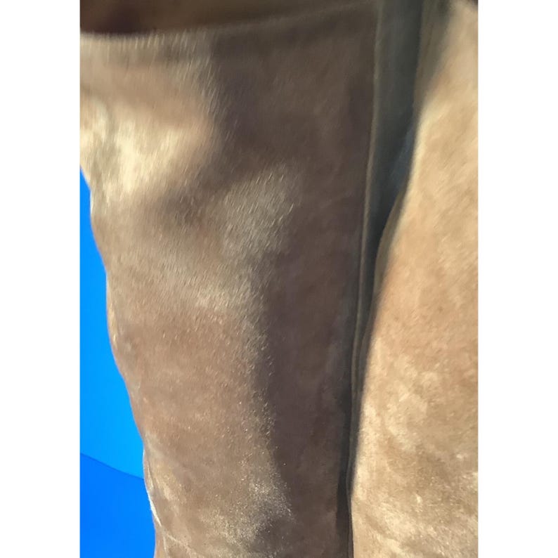 May include: Close-up of a brown suede material. The suede has a soft, textured appearance with subtle variations in color. The image is well-lit, highlighting the details of the fabric. The overall aesthetic is warm and inviting.