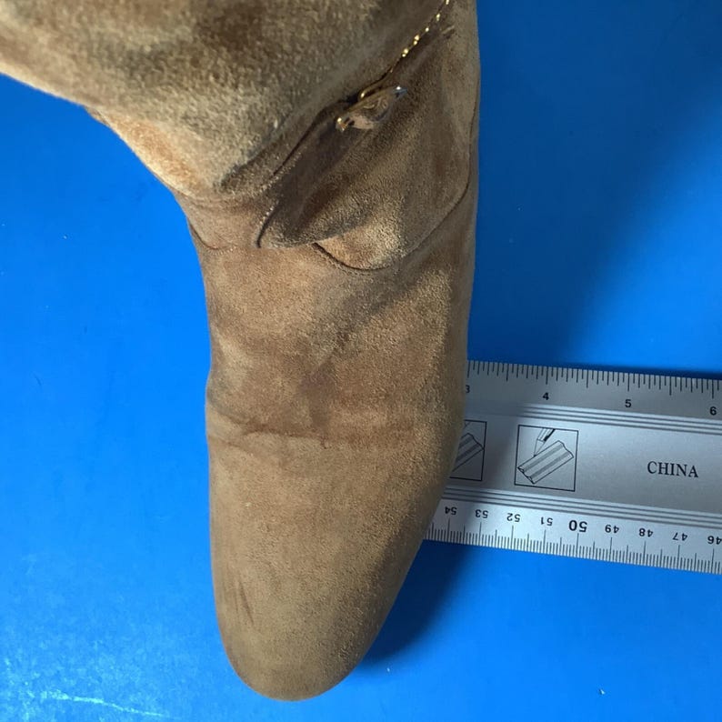 May include: A brown suede boot with a pointed toe and a small gold zipper detail. The boot is measured with a ruler, showing a length of approximately 5 inches.