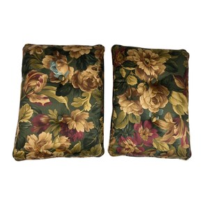 May include: Two rectangular throw pillows with a floral pattern. The pillows feature a dark green background with large flowers in shades of tan, burgundy, and light blue. Each pillow has a button in the center.