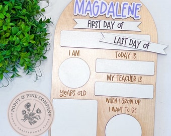 May include: A wooden first and last day of school board with the name "Magdalene" in purple and white. The board has spaces to write "I am", "Today is", "My teacher is", "Things I love", and "When I grow up I want to be".