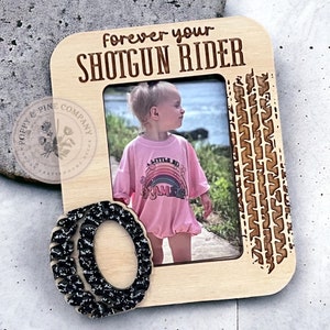 Puede incluir: Marco de fotos de madera con un diseño de banda de rodadura de neumático y el texto "forever your shotgun rider". El marco tiene un recorte para una foto y un diseño de neumático de purpurina negra en la esquina inferior izquierda.