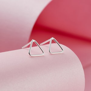 May include: A pair of silver triangle stud earrings. The earrings are simple and minimalist, with a delicate wire design.