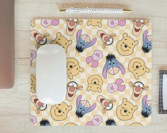 May include: A mouse pad with a checkered pattern featuring Winnie the Pooh and Piglet characters. The characters are in various poses and colors, including yellow, blue, and pink.