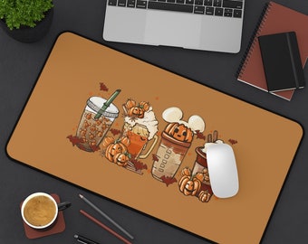 May include: A rectangular orange mousepad featuring a Halloween-themed design. The design includes illustrations of various pumpkin-themed beverages, bats, and pumpkins. A laptop, mouse, and other office supplies are also visible.