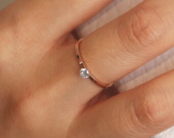 May include: A delicate gold ring with a single, small, clear gemstone. The ring is worn on a finger.
