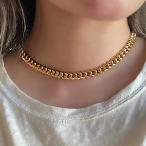 Puede incluir: Un collar de cadena de oro con un estilo de eslabón curb. El collar es grueso y grueso, y lo lleva una persona con una camisa blanca.