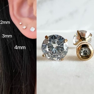 May include: Close-up of three gold stud earrings with clear cubic zirconia stones. The stones are 2mm, 3mm, and 4mm in size.