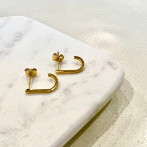 May include: A pair of gold-toned hoop earrings with a slightly curved shape. The earrings are made of a textured metal.