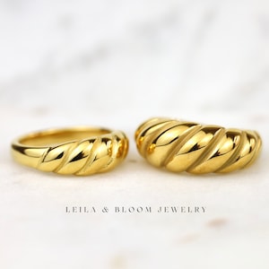 May include: Two gold-toned rings with a twisted, rope-like design. The rings are stacked on top of each other. LEILA & BLOOM JEWELRY is printed below the rings.