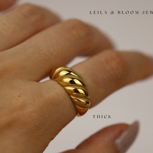 May include: A thick gold ring with a rope-like design. The ring is worn on a finger.