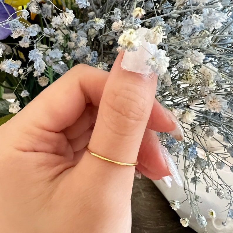 Puede incluir: Un anillo de banda delgado de oro usado en el pulgar.