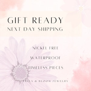Puede incluir: Un fondo de acuarela rosa y blanco con una margarita blanca. El texto "GIFT READY NEXT DAY SHIPPING" est&aacute; en la parte superior de la imagen. El texto "NICKEL FREE WATERPROOF TIMELESS PIECES LEILA & BLOOM JEWELLERY" est&aacute; en la parte inferior de la imagen.