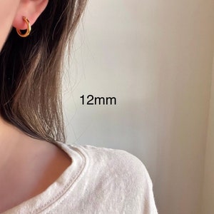 以下が含まれることがあります： 直径12mmのゴールドフープピアス。ピアスは人の耳につけられています。