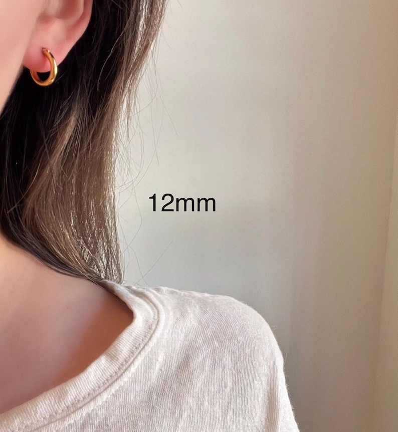 以下が含まれることがあります： 直径12mmのゴールドフープピアス。ピアスは人の耳につけられています。