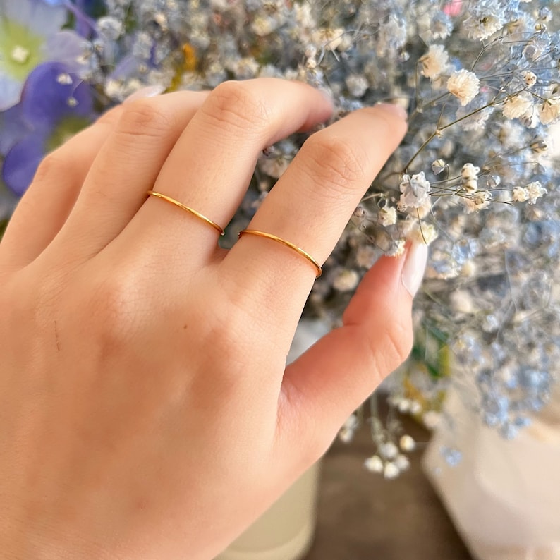 Puede incluir: Dos anillos finos de oro en el dedo de una persona. Los anillos son simples y delicados.