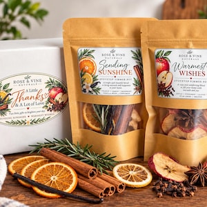 May include: Two kraft paper pouches labeled Rose & Vine Naturals Sending Sunshine and Warmest Wishes stovetop simmer pot ingredients, accompanied by a white gift box, dried orange slices, cinnamon sticks, and star anise.