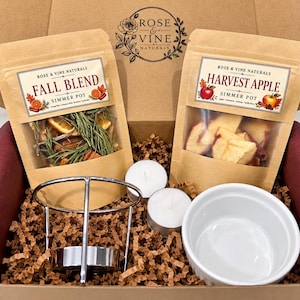 May include: A gift box containing two kraft paper pouches labeled Rose & Vine Naturals Fall Blend and Harvest Apple, a silver metal tea light stand, two white tea light candles, and a small white ceramic ramekin nestled in brown paper filler.