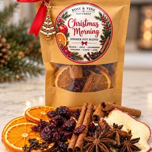 May include: A brown paper pouch labeled Rose & Vine Naturals Christmas Morning Simmer Pot Blend, tied with a red ribbon and a Christmas tree charm. The pouch contains dried orange slices, cinnamon sticks, cranberries, and star anise.