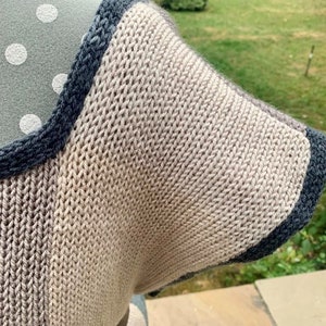 May include: A close-up of a knitted garment with a brown and blue color scheme. The garment has a textured knit pattern and a contrasting blue trim.