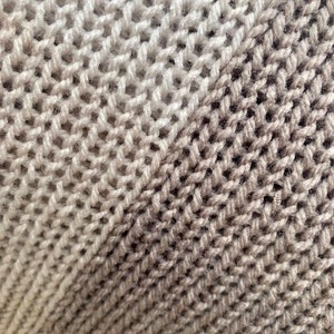 May include: Close-up of a knitted fabric with a gradient of beige and brown colors. The fabric is made of a soft, textured yarn and has a diagonal pattern.