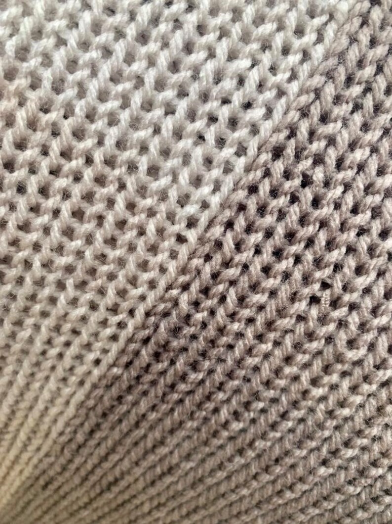 May include: Close-up of a knitted fabric with a gradient of beige and brown colors. The fabric is made of a soft, textured yarn and has a diagonal pattern.