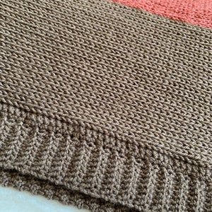 May include: A brown and coral striped knitted blanket with a textured weave. The blanket is folded in half and the edges are visible.