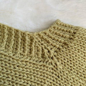 May include: Close-up of a knitted sweater with a green color. The sweater has a ribbed texture and a high neckline.