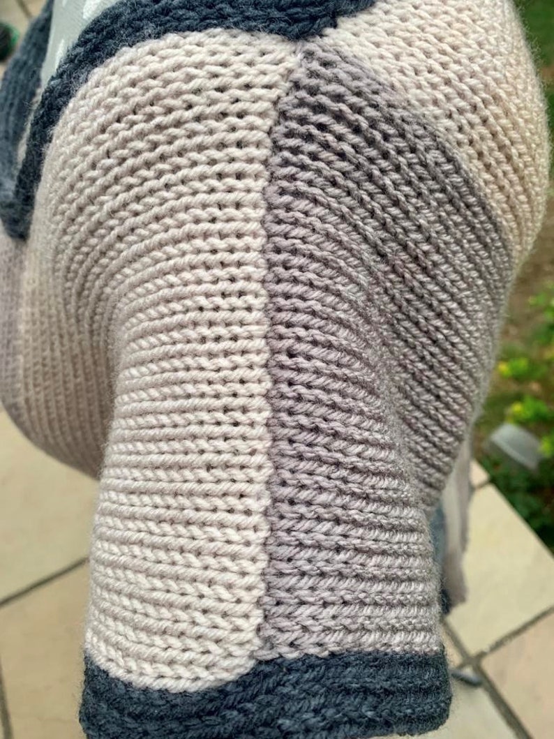 May include: Close-up of a knitted fabric with a gradient of colors, from light gray to dark gray. The fabric is made of soft yarn and has a textured surface. The fabric is folded over itself, creating a layered effect.