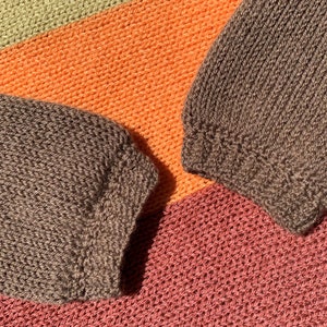 May include: Close-up of a brown knitted fabric with a striped pattern in orange, green, and pink.