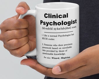 May include: White ceramic mug with a black and white design. The mug features a definition of the word "Clinical Psychologist" with a humorous tone. The text reads: "(kli-nuh-kl sy-ka-luh-jihst) noun. 1. Like a normal Psychologist but MUCH cooler. 2. Someone who does precision guesswork based on unreliable data provided by those of questionable knowledge. See also: Wizard, Magician"