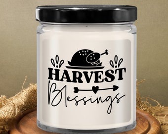 May include: A white candle jar with a black lid and a label that says "HARVEST Blessings" with a black silhouette of a turkey on a plate and two hearts with an arrow pointing to the right.