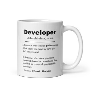 Puede incluir: Taza de café de cerámica blanca con una definición en blanco y negro de la palabra "Desarrollador" impresa en ella. La definición dice: "(duh-veh-luh-pr) sustantivo. 1. Alguien que resuelve problemas que no sabías que tenías de maneras que no entiendes. 2. Alguien que hace conjeturas precisas basadas en datos poco fiables proporcionados por personas con conocimientos cuestionables. Ver también: Mago, Mago"