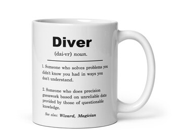 Puede incluir: Taza de café de cerámica blanca con un diseño en blanco y negro. La taza presenta la palabra "Diver" con una definición que dice: "(dai-vr) sustantivo. 1. Alguien que resuelve problemas que no sabías que tenías de maneras que no entiendes. 2. Alguien que hace conjeturas precisas basadas en datos poco fiables proporcionados por personas con conocimientos cuestionables. Ver también: Mago, Mago"
