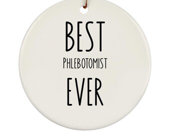 May include: A white, round ceramic ornament with the text "BEST PHLEBOTOMIST EVER" in black, bold letters. The ornament has a small hole at the top with a gold string for hanging. A simple, yet thoughtful gift.
