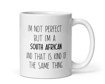 Könnte beinhalten: Eine weiße Keramik-Kaffeetasse mit schwarzem Text, der lautet: "Ich bin nicht perfekt, aber ich bin ein Südafrikaner, und das ist irgendwie dasselbe."
