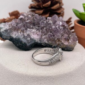 May include: A silver ring with a large, clear, round gemstone surrounded by smaller, clear gemstones. The ring has a delicate, intricate design.