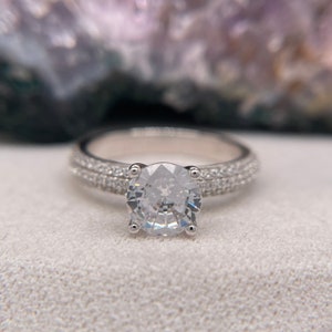 May include: A silver engagement ring with a large, round, clear centre stone and a double row of smaller stones around the band.