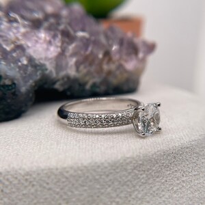 May include: A silver engagement ring with a round centre stone and a band that is accented with small diamonds.