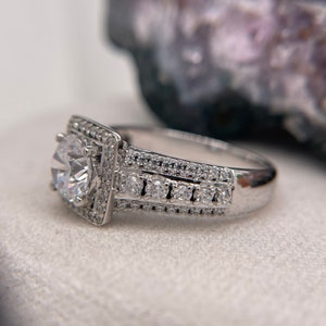 May include: A silver engagement ring with a large, round, clear center stone surrounded by smaller stones. The band is also set with smaller stones.