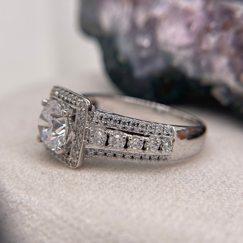 May include: A silver engagement ring with a large, round, clear center stone surrounded by smaller stones. The band is also set with smaller stones.